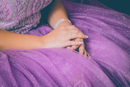 Close-up of hands resting gracefully on a purple sparkling dress, showcasing elegance.