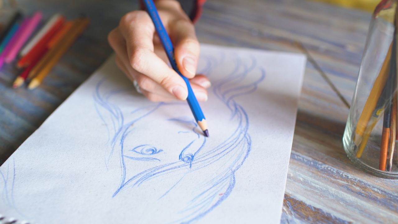 Close-up of a hand drawing a portrait using color pencils on paper.